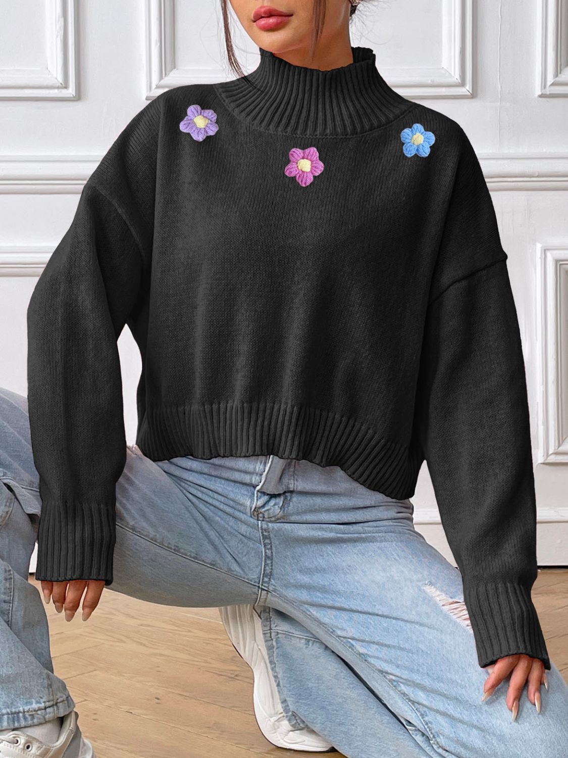 Black cropped turtleneck knit sweater with embroidered floral details and ribbed cuffs and hem.