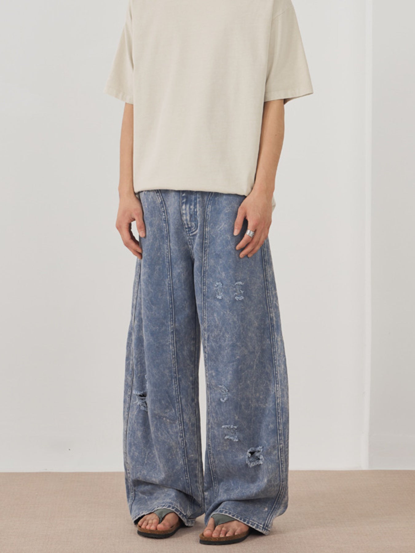 Men's distressed wide-leg acid wash denim jeans in blue with ripped details.