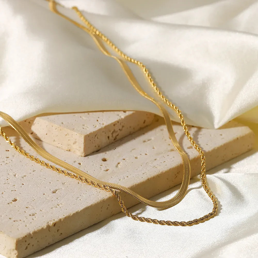 Gold serpentine and rope chain necklaces layered on textured blocks.