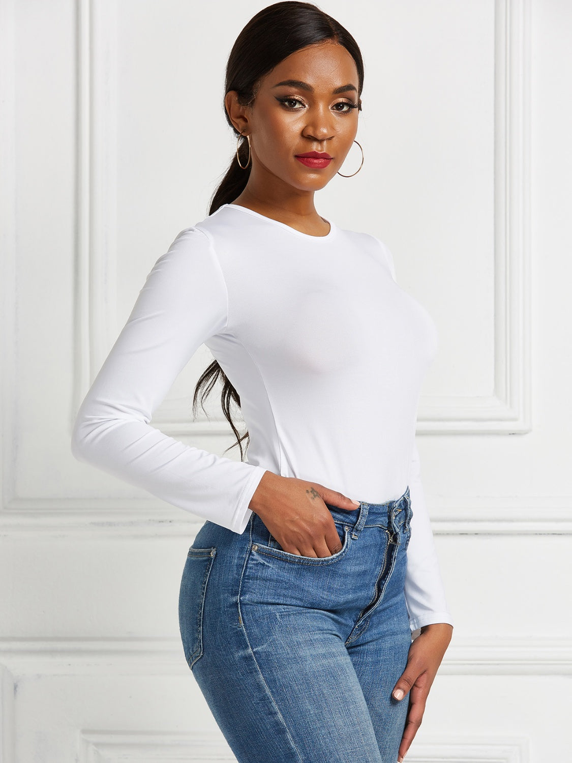 White long sleeve ribbed bodysuit with crew neck, tucked into blue jeans.