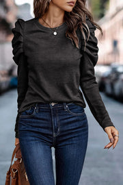 Black knit top with crew neck and puffed long sleeves, styled with dark wash jeans.