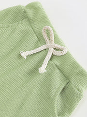 Green waffle knit children's pants with a decorative white drawstring bow.