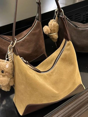 Tan suede crossbody bag with zipper closure and brown trim, featuring a teddy bear charm.
