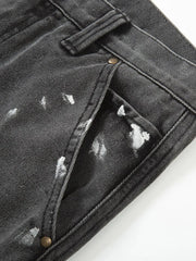 Dark gray bootcut jeans with white paint splatters and brass button details.