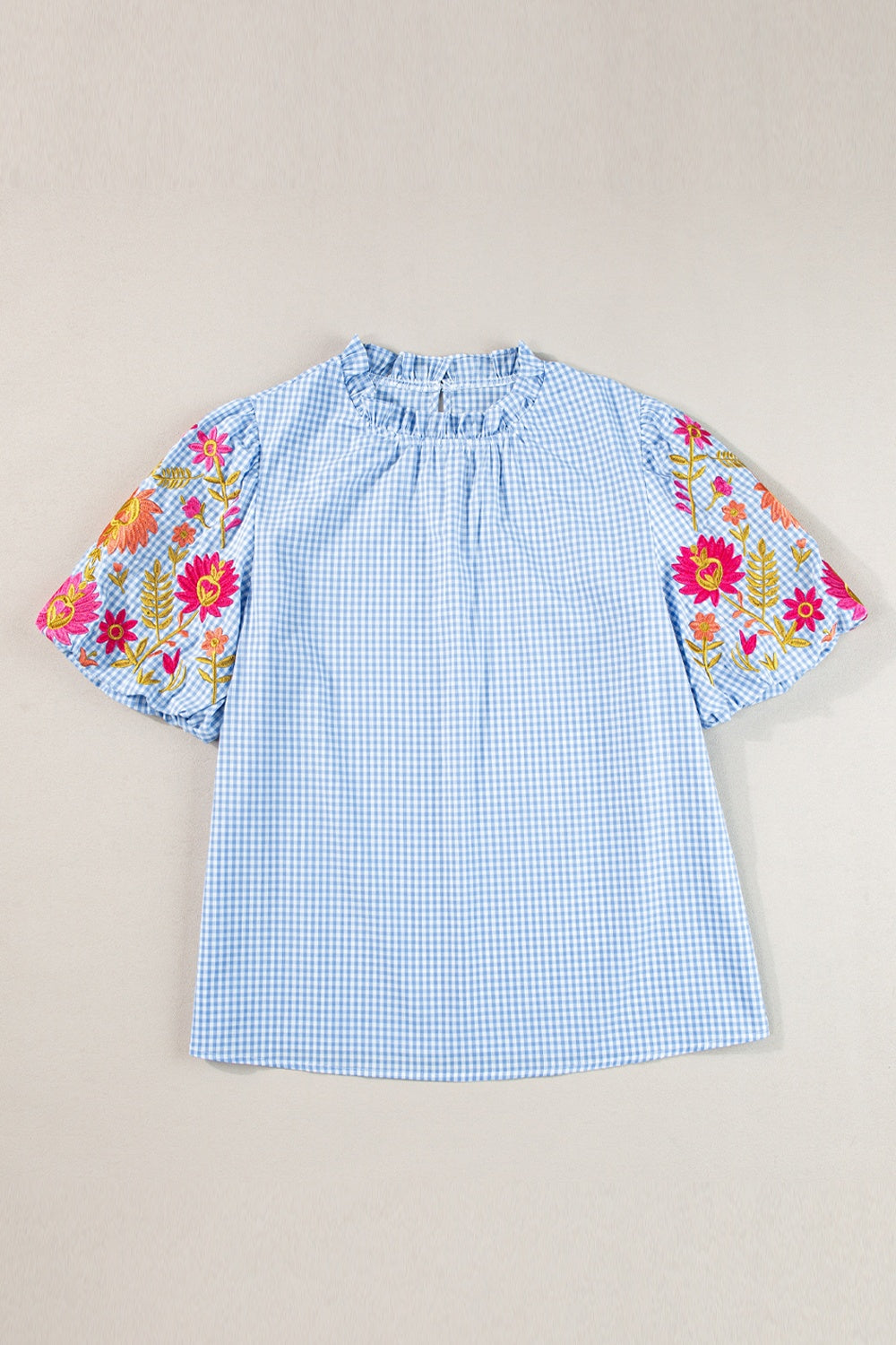 Light blue gingham blouse with embroidered floral sleeves and ruffled neckline.