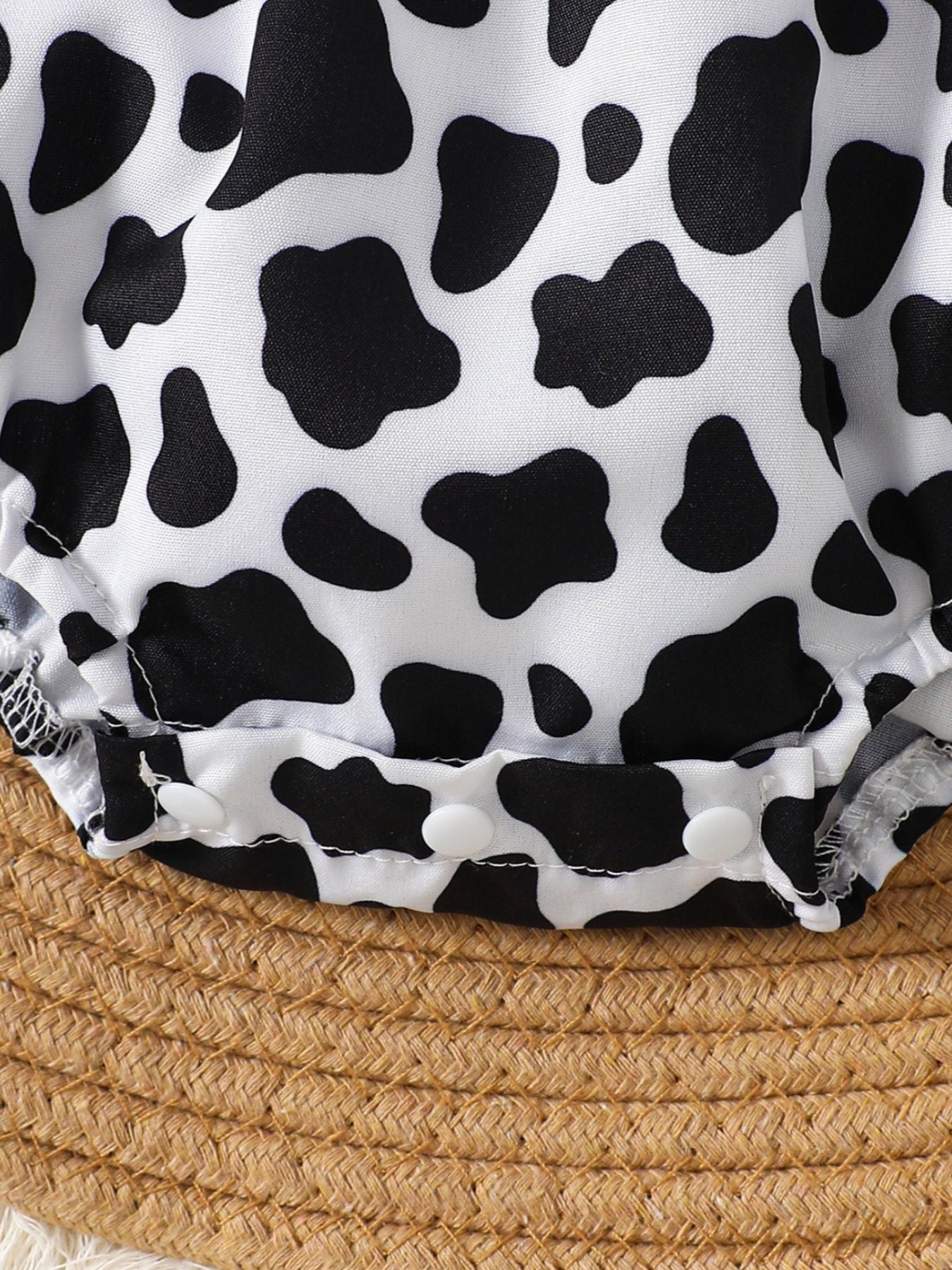 Baby one-piece romper with cow print, white with black spots, and white snap closures.