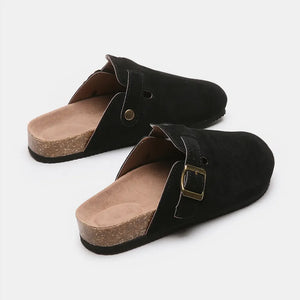 Black suede clog slides with cork sole and adjustable buckle detail.