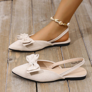 Beige bow accent slingback slip-on flats with a pointed toe and ankle strap.