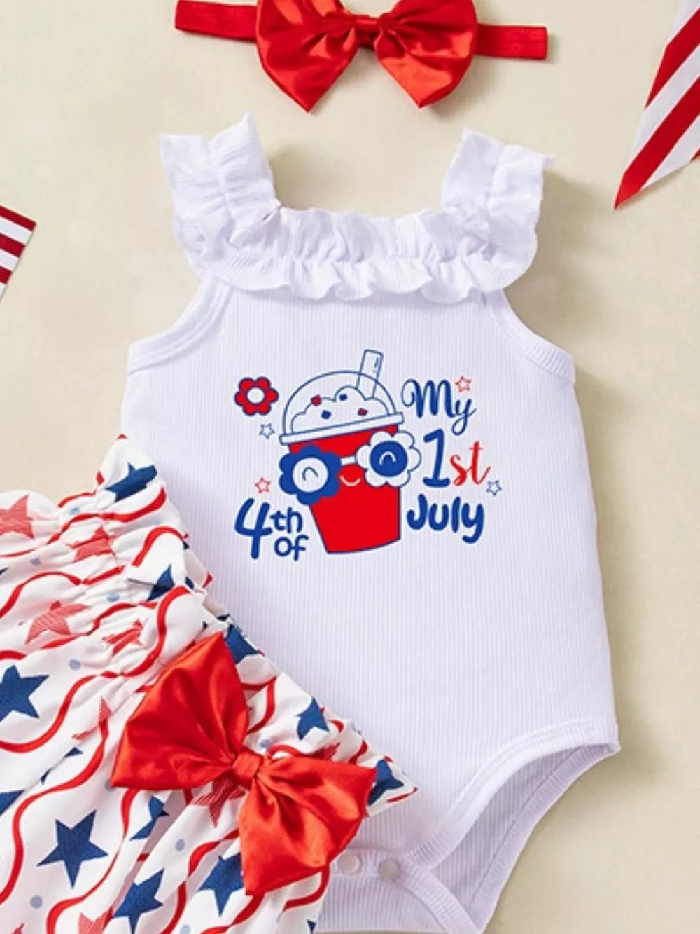 White baby bodysuit with ruffled neckline and "My 1st 4th of July" graphic, paired with star-print bloomer shorts and red