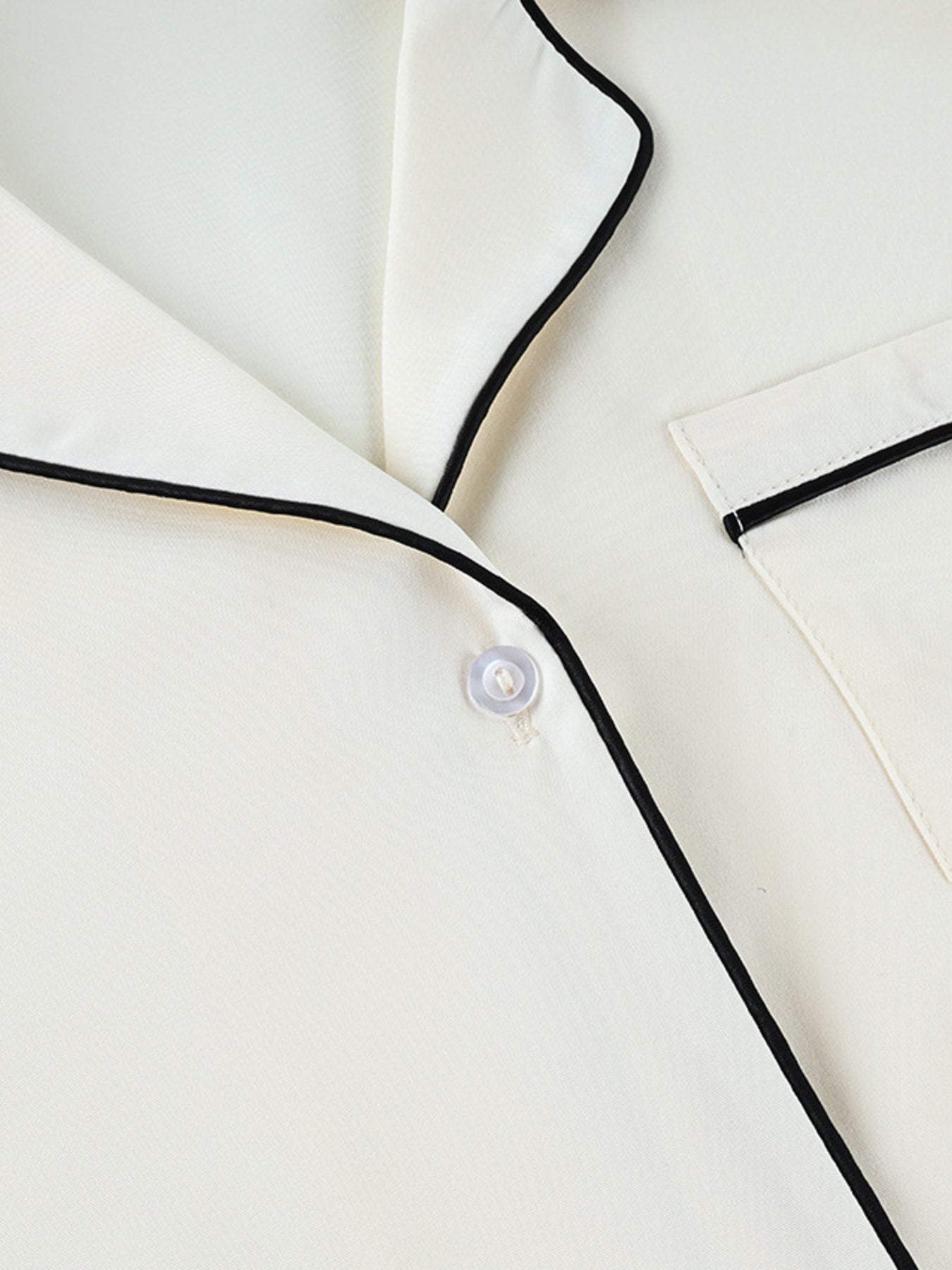 Button-up pajama top in cream with black piping and a single button closure.