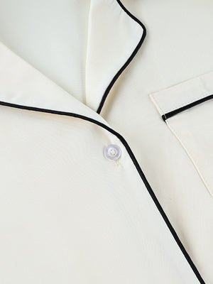 Button-up pajama top in cream with black piping and a single button closure.
