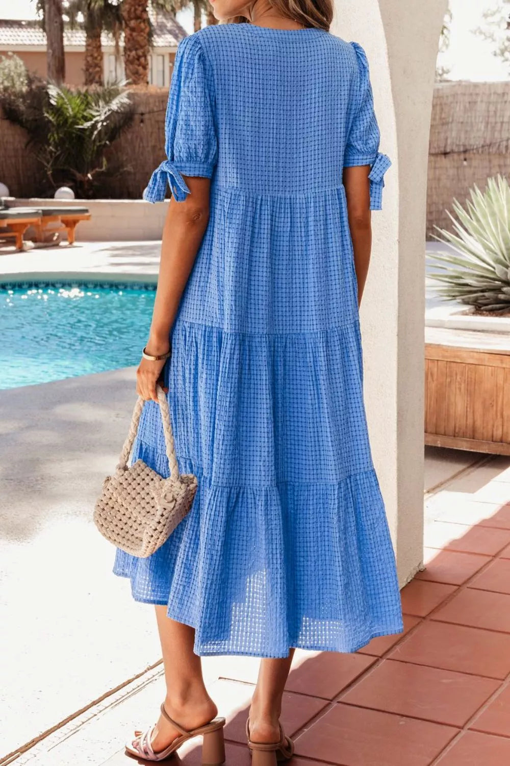 Blue tiered midi dress with short sleeves, notched neckline, and tie details.