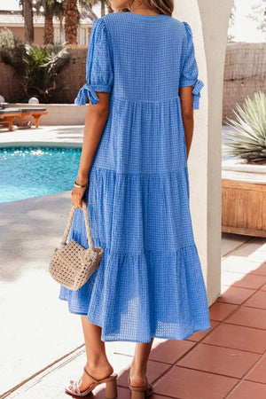 Blue tiered midi dress with short sleeves, notched neckline, and tie details.