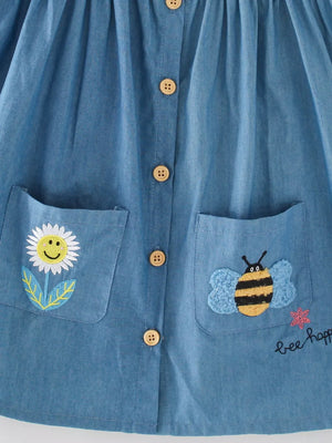 Denim dress with bee and flower embroidery, button front, and pockets.