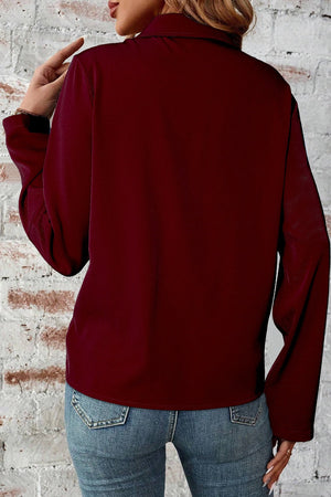 Burgundy zip-front blouse with long sleeves and collar, styled with jeans.