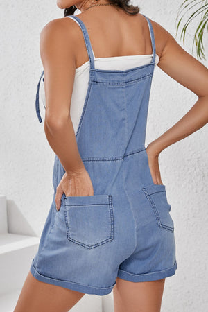 Denim romper with adjustable straps and rolled hem shorts in medium wash.