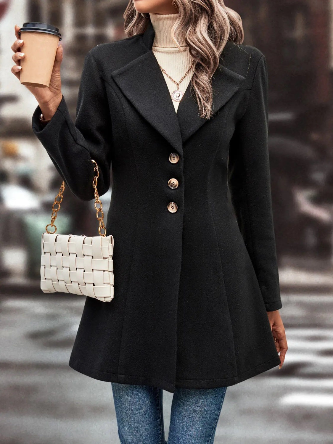 Black wool blend coat with button front and flared hem, styled with a white woven bag.