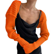 Orange ribbed knit shrug with extended sleeves styled over a black slip dress.
