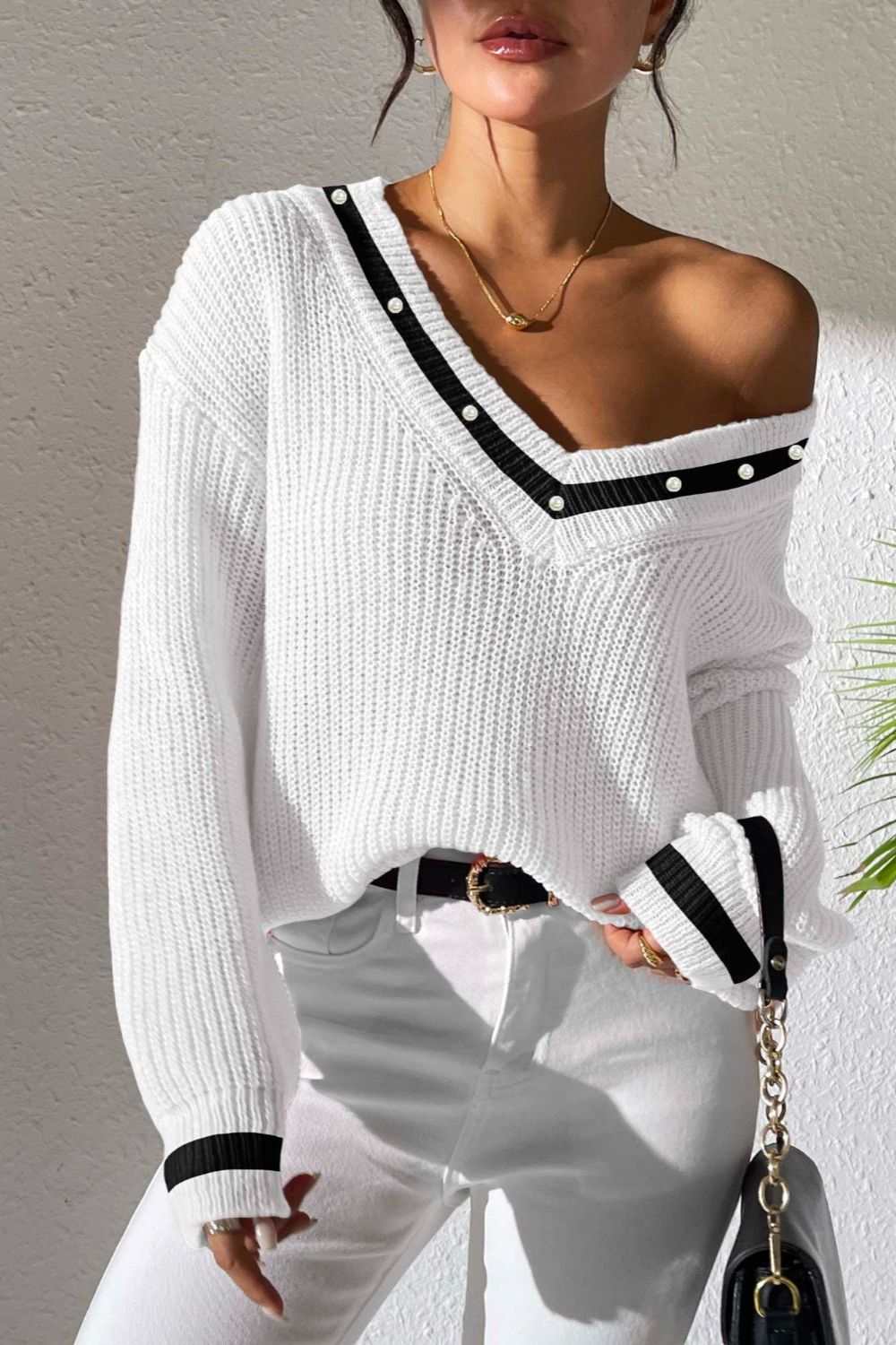 White ribbed knit sweater with V-neck, black trim, and pearl details on neckline and cuffs.