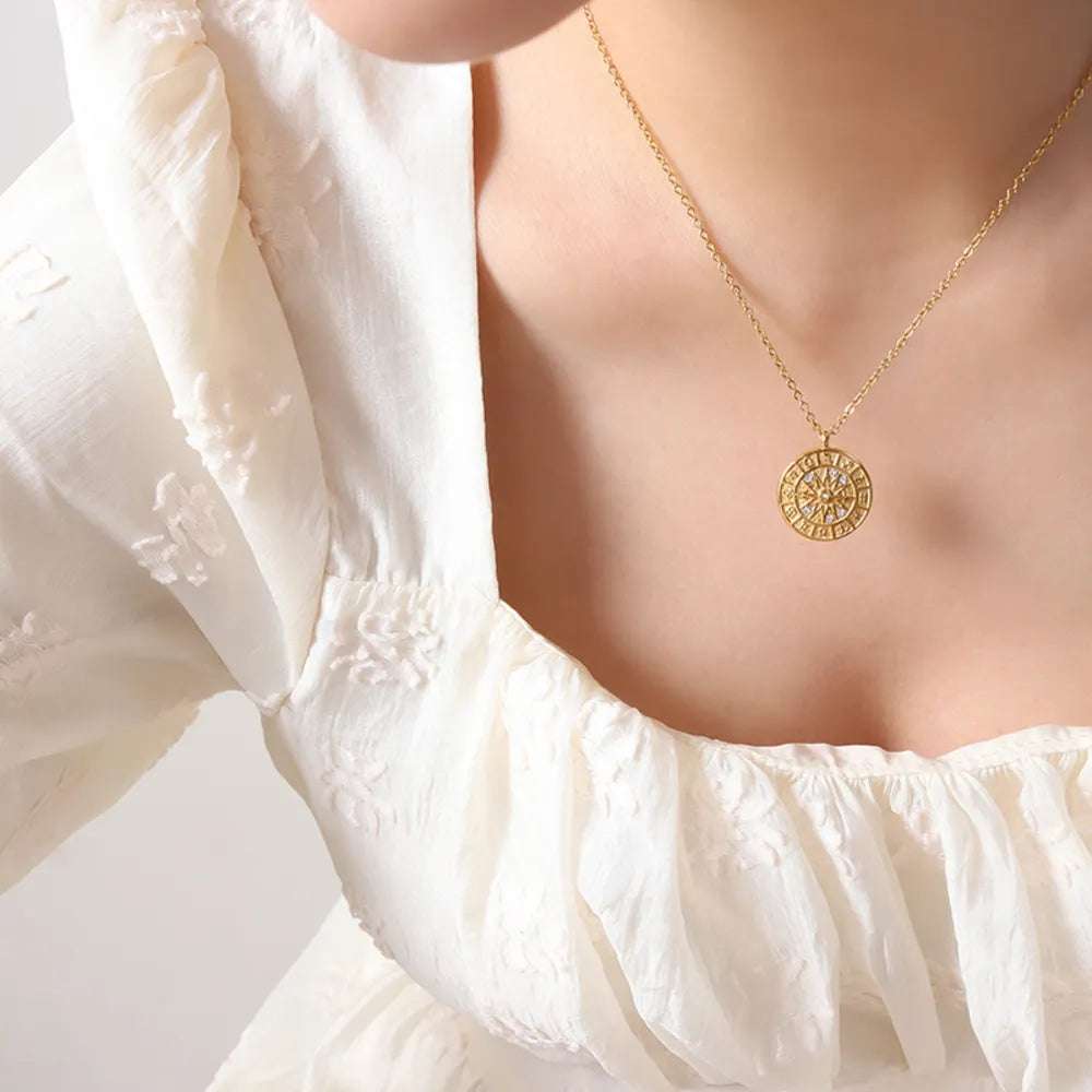 Gold zodiac compass pendant necklace with clear stones on a delicate chain.
