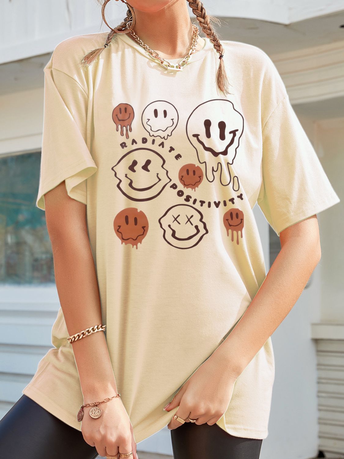 Tan oversized graphic tee with melting smiley faces and "Radiate Positivity" text.
