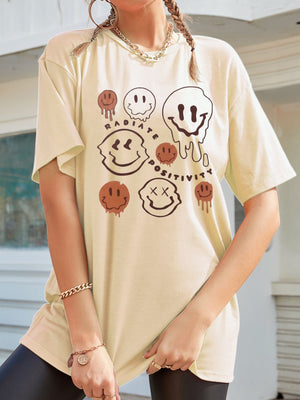 Tan oversized graphic tee with melting smiley faces and "Radiate Positivity" text.