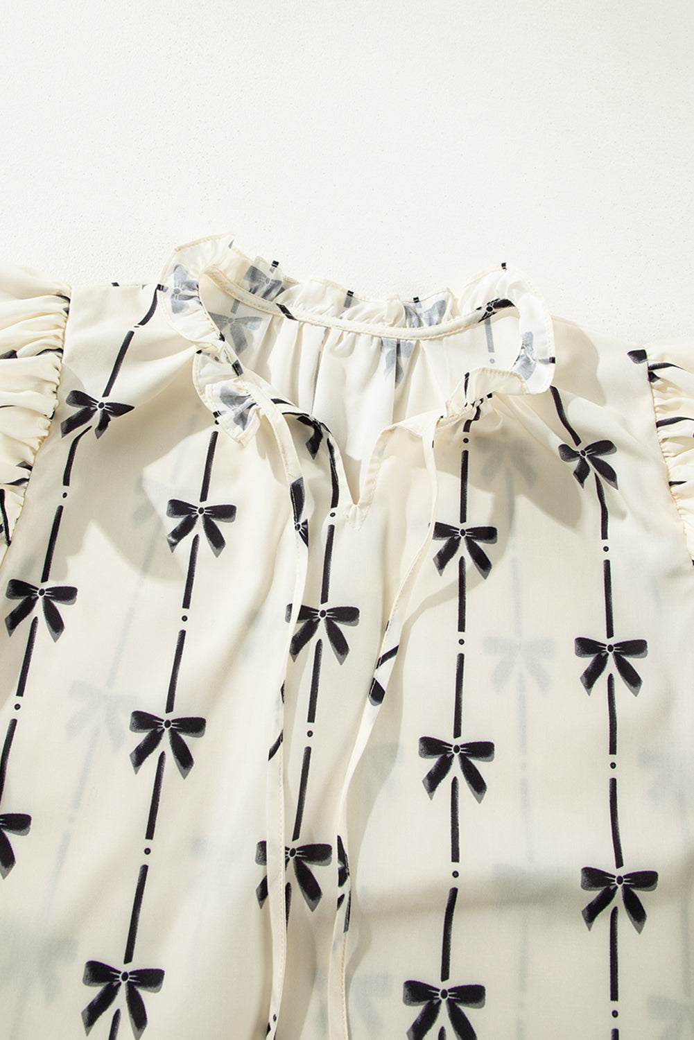Ivory blouse with black bow print, ruffled neckline and sleeves, and tie detail.