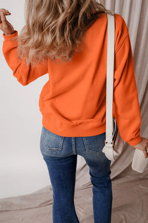 Orange graphic sweatshirt with crew neck and long sleeves, styled with jeans.