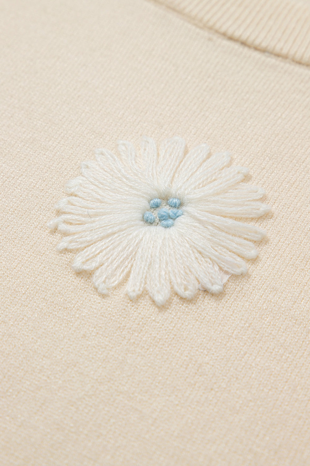 Ivory knit cardigan with a white daisy appliqué and blue center detail.