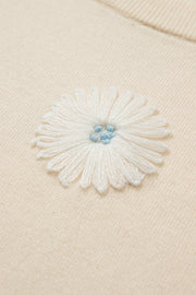 Ivory knit cardigan with a white daisy appliqué and blue center detail.