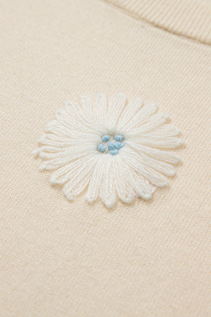 Ivory knit cardigan with a white daisy appliqué and blue center detail.