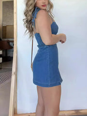 Blue denim mini dress with tie straps, smocked waist, and side slit hem.