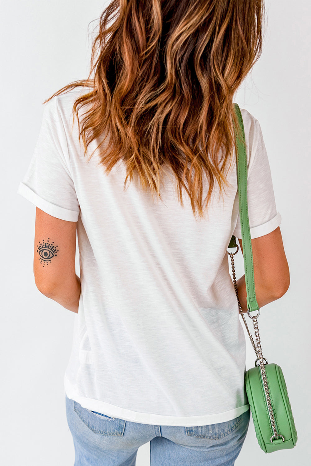 White graphic tee with rolled sleeves and an eye tattoo on the arm.