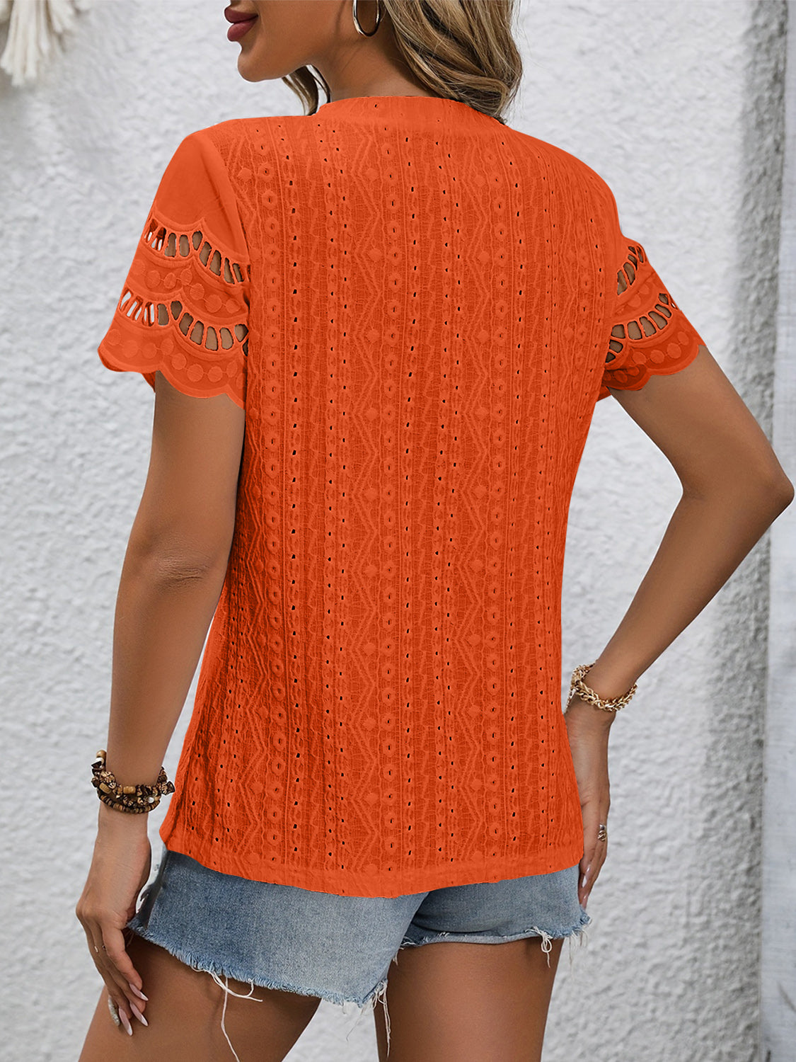 Orange eyelet blouse with scalloped short sleeves and textured pattern.