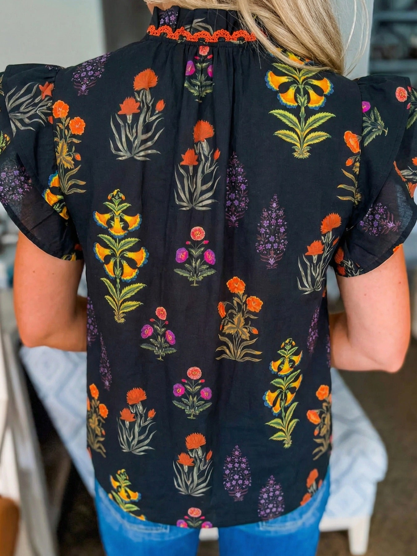 Black cotton maternity shirt with floral print, ruffled sleeves, and orange trim neckline.