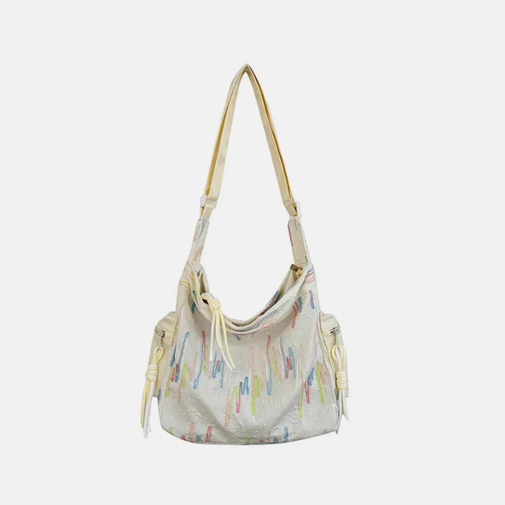 Ivory slouchy shoulder bag with colorful embroidered abstract lines and tassel details