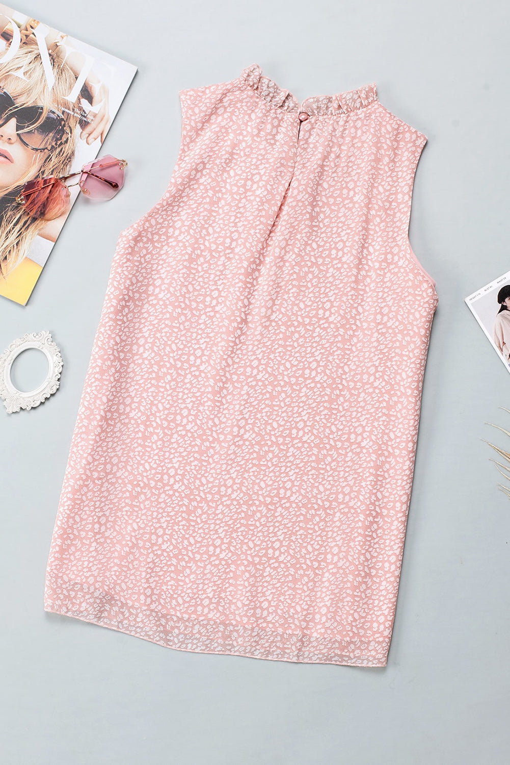 Blush pink sleeveless blouse with ruffled neckline and allover print.
