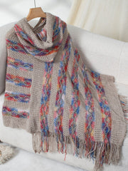 Textured knit hooded cape in beige with colorful striped and cable knit details and fringe.