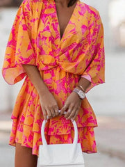Tropical tiered mini dress in orange and fuchsia pink with surplice neckline and flutter sleeves.