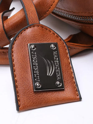 Brown leather half-moon bag detail with metal logo plate and stitching.