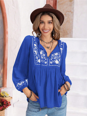 Royal blue peasant blouse with white floral embroidery on yoke and sleeves, gathered bodice, and tie neck.