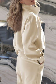Beige quarter-zip sweatshirt with high collar and jogger pants with pockets.