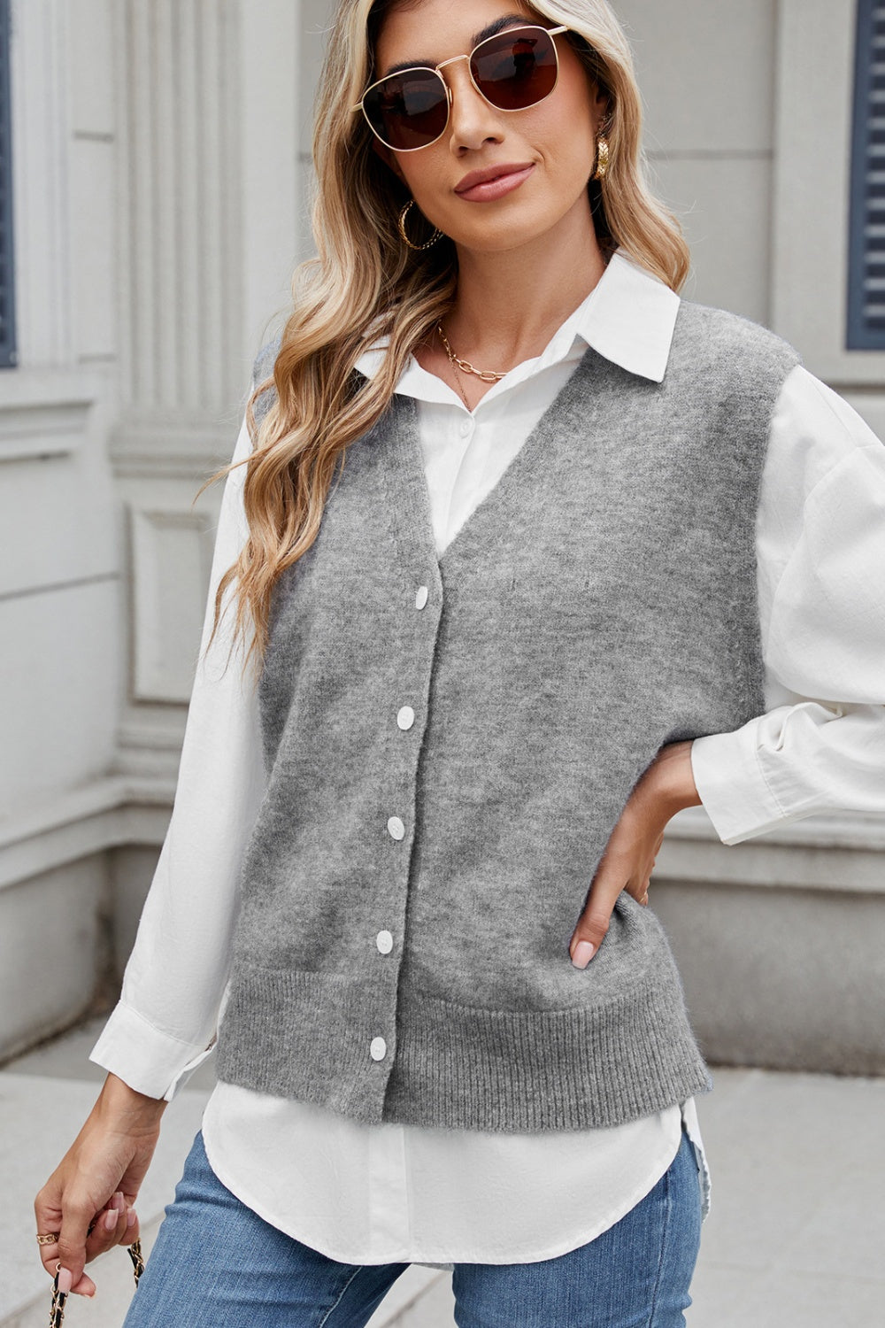 Grey button-front knit vest with V-neck and ribbed hem, styled over a white shirt.