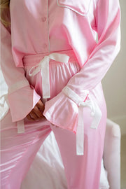 Blush pink silk pajamas with ruffle bell sleeves and white tie details.