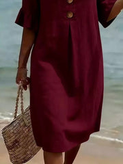 Burgundy ruffled sleeve dress with button detail and a woven tote bag on the beach.