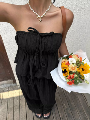 Black tube top with tiered ruffles and tie detail, paired with wide-leg pants.