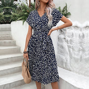 Dark blue midi dress with white dots, V-neck, short sleeves, belted waist, and pleated skirt.