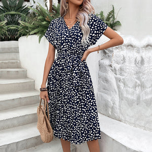 Dark blue midi dress with white dots, V-neck, short sleeves, belted waist, and pleated skirt.