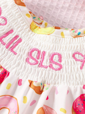 White smocked baby one-piece with donut print and pink embroidery.