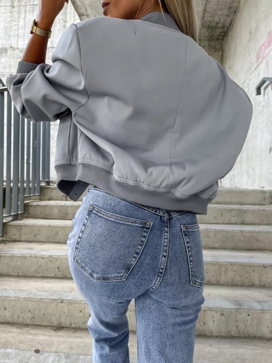 Gray faux leather bomber jacket with sculpted sleeves and ribbed trim, styled with denim jeans.